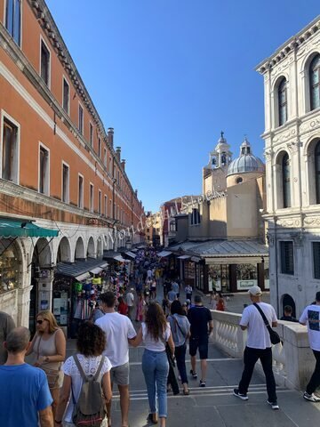 Rue animée à Venise, Italie, avec des bâtiments colorés et des boutiques sur les côtés, sous un ciel bleu.