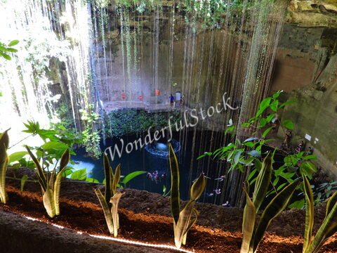 Cenote avec des plantes et des cascades d'eau, situé à Ik Kil, Mexique. Des visiteurs se trouvent près de l'eau.