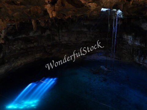 Cenote avec des reflets lumineux, Mexique. Des stalactites se forment au plafond, tandis que l'eau claire révèle un fond rocheux.