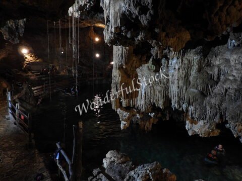 Cenote Samula au Mexique, avec des stalactites et des lumières au plafond, entouré d'eau et de visiteurs.