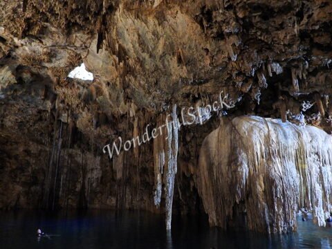 Cénote Samula au Mexique, avec des formations rocheuses et des stalactites visibles dans une grotte au-dessus d'une eau sombre.
