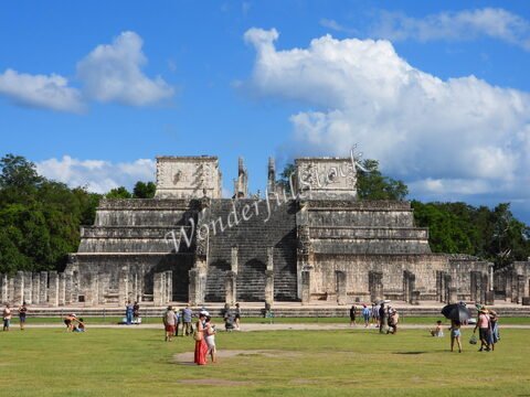 Pyramide de Chichén Itzá au Mexique, entourée de visiteurs, avec des nuages blancs en arrière-plan et une végétation dense.