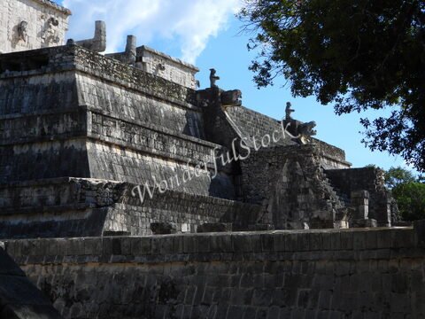 Pyramide en pierre à Itza, Mexique, avec des sculptures distinctives sur les murs et un ciel partiellement nuageux.