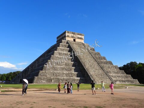 Pyramide à Chichén Itzá, Mexique, avec des visiteurs se tenant autour et un ciel bleu en arrière-plan.