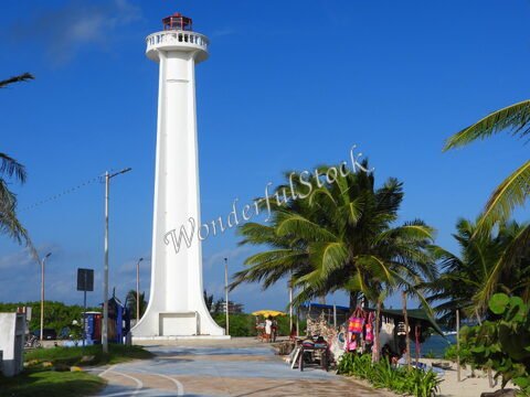 Phare blanc sur la promenade à Mahahual, Mexique, entouré de palmiers et de stands de marché.