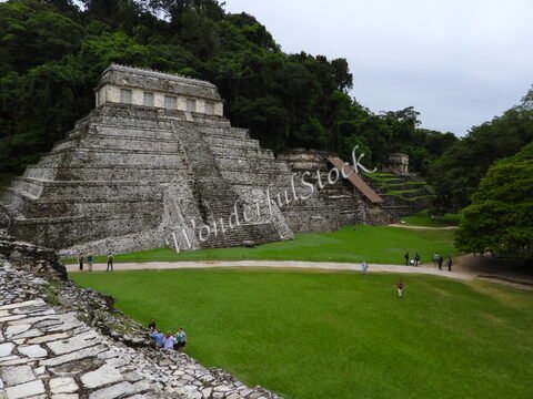 Ruines mayas entourées de verdure à Palenque, Mexique, avec des escaliers en pierre et des visiteurs sur un terrain herbeux.