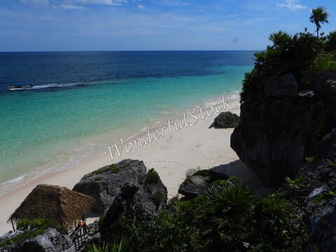 Plage de sable fin et mer turquoise à Tulum, Mexique, avec des rochers et une cabane en palmier.
