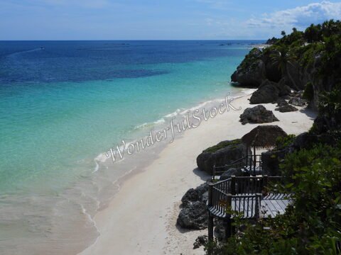 Plage de sable blanc et eaux turquoise à Tulum, Mexique, avec quelques rochers et une structure en bois sur la côte.
