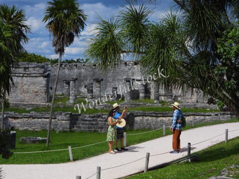 Ruines de Tulum, au Mexique, avec des visiteurs portant des chapeaux, entourés de palmiers et d'une végétation verdoyante.