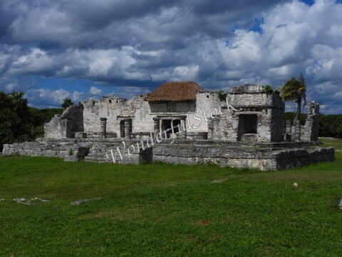 Ruines anciennes avec toiture en chaume, situées à Tulum, Mexique, entourées de verdure et d'un ciel nuageux.