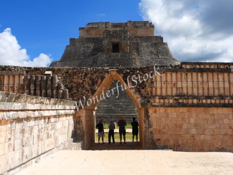 Ruines d'Uxmal au Mexique, avec un groupe de personnes se tenant sous un arc, et une pyramide en arrière-plan.