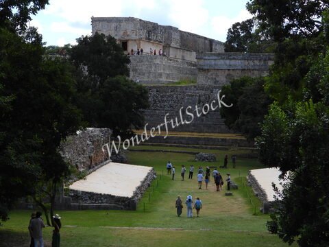 Ruines d'Uxmal au Mexique, avec des visiteurs se déplaçant sur une pelouse entourée d'arbres et de structures anciennes.