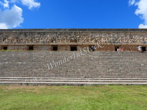 Mur ancien avec motifs géométriques et escaliers, situé à Uxmal, Mexique. Ciel bleu avec quelques nuages.