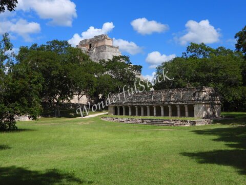 Ruines mayas entourées de verdure à Uxmal, Mexique, avec un bâtiment à colonnes et une pyramide en arrière-plan.