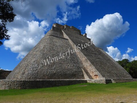 Pyramide à Uxmal, Mexique, avec des nuages en arrière-plan et une végétation verdoyante au premier plan.