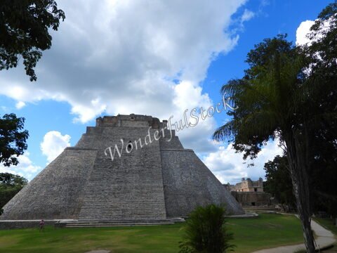 Pyramide d'Uxmal au Mexique, entourée d'arbres et d'un ciel nuageux.