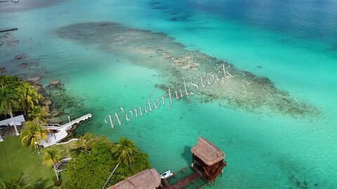 Bacalar, Mexique, avec des eaux turquoise et des formations rocheuses visibles sous l'eau, entouré de palmiers et de structures en bois.