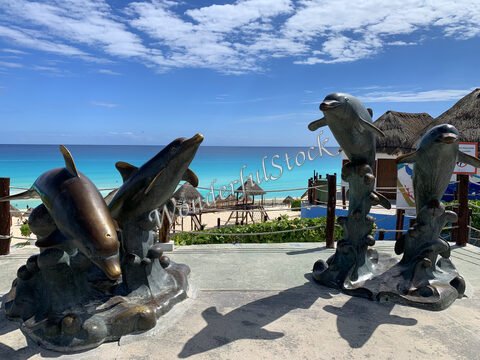 Statues de dauphins sur une plage à Cancun, Mexique, avec une mer turquoise en arrière-plan et des palapas.