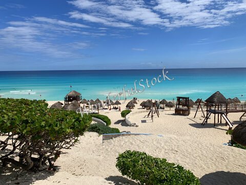 Plage de sable avec des palapas à Cancun, Mexique, et une mer turquoise sous un ciel partiellement nuageux.