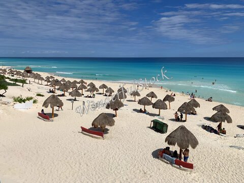 Plage avec parasols à Cancún, Mexique, et des personnes se baignant dans l'eau turquoise.