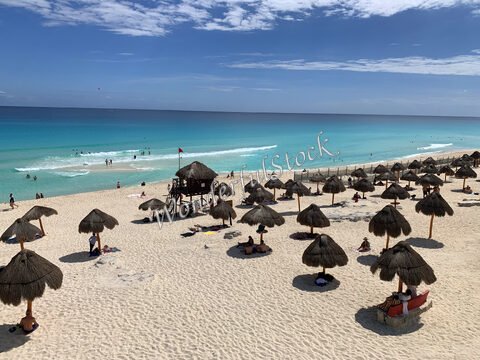 Plage de sable avec des parasols en chaume à Cancun, Mexique, et des baigneurs dans l'eau turquoise.