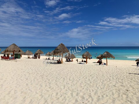 Plage de Cancún au Mexique, avec des parasols en paille et des personnes se détendant sur le sable blanc.