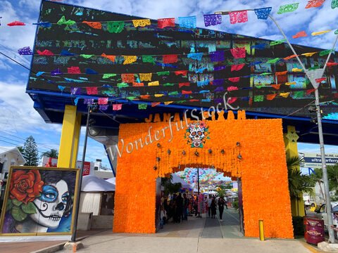 Entrée décorée avec des fleurs orange et des banderoles colorées à Cancun, Mexique, avec une fresque de crâne sur un mur.