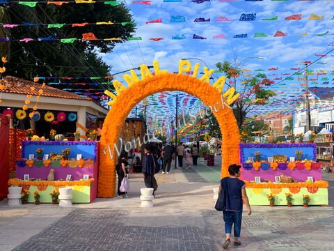 Arche décorée de fleurs et de guirlandes colorées à Cancun, Mexique, avec des personnes marchant dans une rue animée.