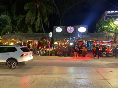 Bar avec éclairage coloré et décoration festive à Cancun, Mexique, entouré de palmiers et de clients.