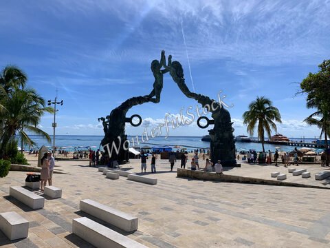 Sculpture en bronze à Playa del Carmen, Mexique, avec des palmiers et des personnes se promenant sur la plage.