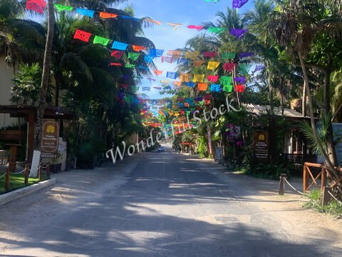 Des décorations colorées en papier sont suspendues au-dessus d'une rue à Tulum, au Mexique, bordée de palmiers et de bâtiments.