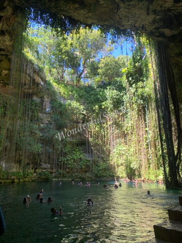 Cenote Ik Kil au Mexique, avec des visiteurs dans l'eau et des parois verdoyantes entourées de végétation.