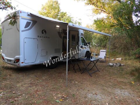 Camping-car stationné dans la nature en Ardèche, France, avec une table et des chaises à côté.
