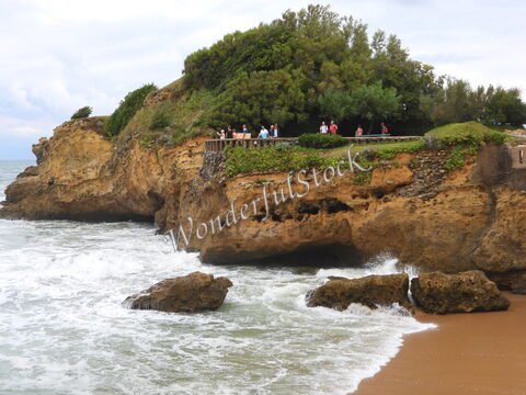 Falaises surplombant la mer à Biarritz, France, avec des personnes sur un chemin surplombant la côte et des vagues s'écrasant sur les rochers.