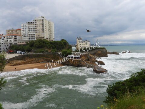 Plage et vagues à Biarritz, France, avec des bâtiments en arrière-plan et un oiseau en vol.