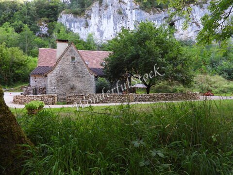 Maison en pierre avec un toit en tuiles, entourée de verdure à Bouziès, France, près de falaises blanches.