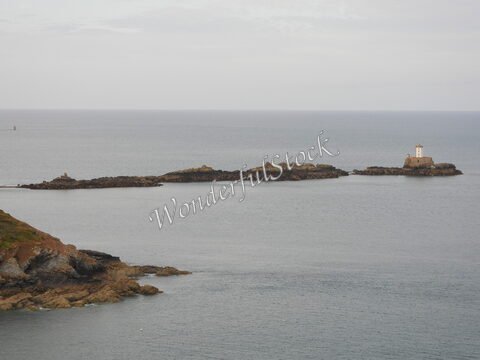 Un phare se dresse sur un rocher au Cap Fréhel, en Bretagne, France, entouré par la mer calme et des formations rocheuses.