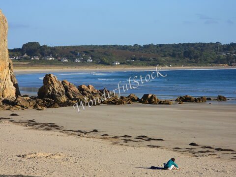 Plage de Crozon en Bretagne, France, avec des rochers et une personne assise sur le sable.