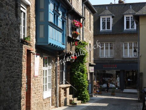 Rue pavée avec des maisons en pierre et un balcon bleu fleuri à Dinan, France.