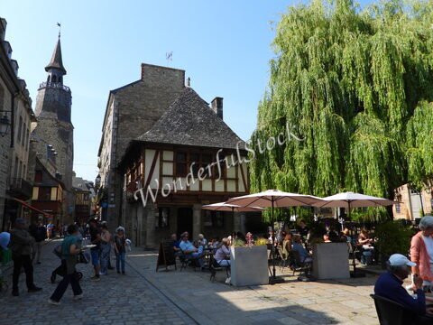 Terrasse animée avec des parasols, maisons à colombages et la tour d'une église à Dinan, France.