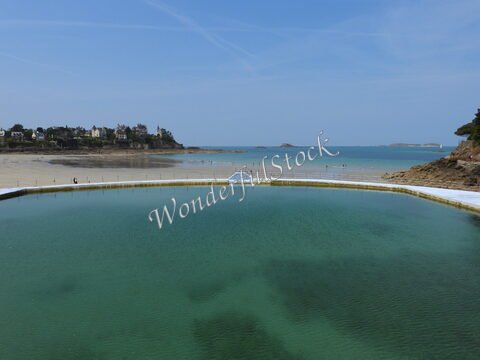 Baignade dans une piscine naturelle à Dinard, France, avec des maisons en arrière-plan et la mer à l'horizon.