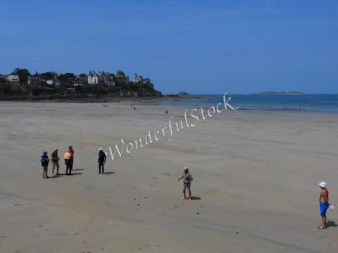 Plage à Dinard, France, avec des personnes jouant à la pétanque et des maisons en arrière-plan.