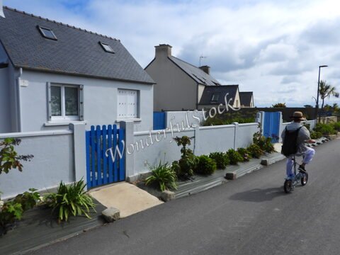 Un cycliste passe devant des maisons blanches avec une clôture bleue sur l'île de Batz, en Bretagne, France.
