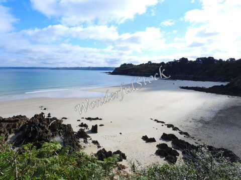 Plage de Locquirec en Bretagne, France, avec des rochers sur le rivage et un ciel partiellement nuageux.