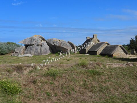 Maisons en pierre avec toits de chaume près de rochers à Meneham, Bretagne, France. Ciel dégagé et végétation environnante.