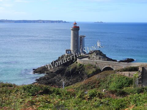 Phare du Petit Minou en Bretagne, France, surplombant la mer avec un voilier à proximité et des rochers environnants.