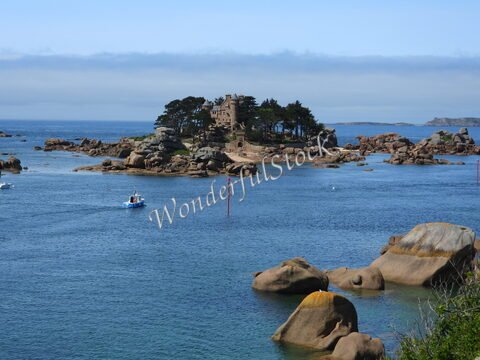 Une maison en pierre se trouve sur une île entourée de rochers à Ploumanach, en Bretagne, France, avec des bateaux naviguant sur l'eau.