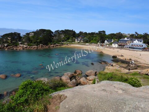 Plage de Ploumanach en Bretagne, France, avec des rochers et des maisons sur le rivage sous un ciel dégagé.
