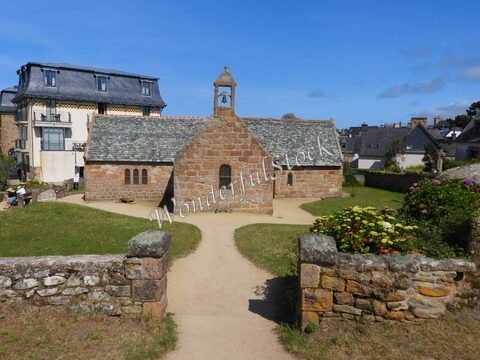 Chapelle en pierre avec un toit en ardoise à Ploumanach, France, entourée de verdure et de bâtiments traditionnels.