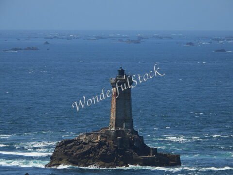 Phare sur un rocher à la Pointe du Raz, Bretagne, France, avec la mer et des îlots en arrière-plan.
